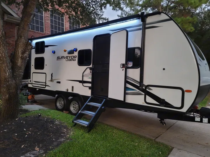 Spacious RV rental, a white Surveyor Legend travel trailer, ready for adventure with its lighted awning & steps.. Forest River Surveyor 2021