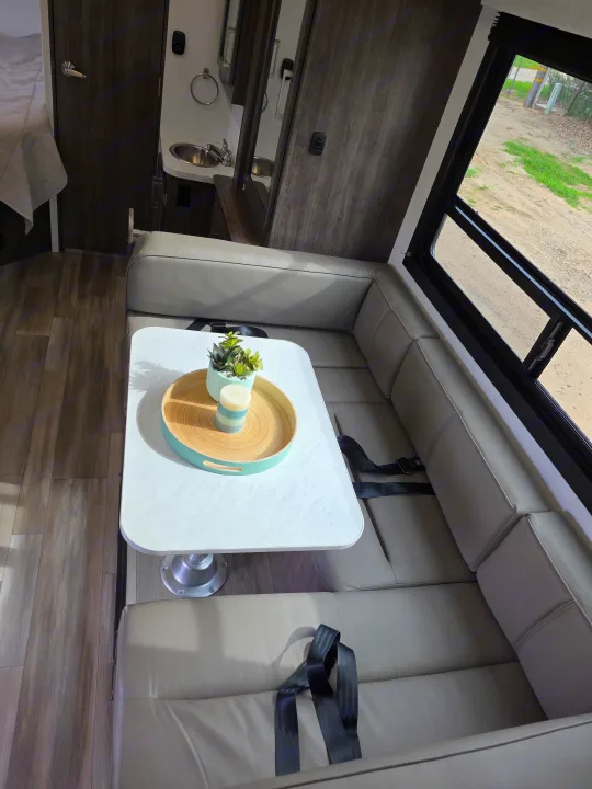 Interior of an RV rental: a cozy U-shaped dinette with a table, seatbelts, and a window offering a glimpse of the outdoors.. Jayco Redhawk SE 2026