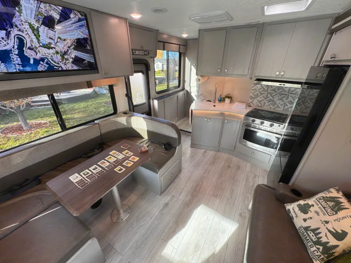Modern rv rental interior: dinette with cards, full kitchen, TV, and outdoor views. Perfect for a cozy road trip adventure.. Forest River Coachmen Freelander 2026
