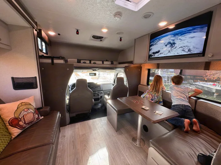 Inside an rv rental: two children play cards at the dinette, watching TV with Earth, and gazing out the window.. Forest River Coachmen Freelander 2026