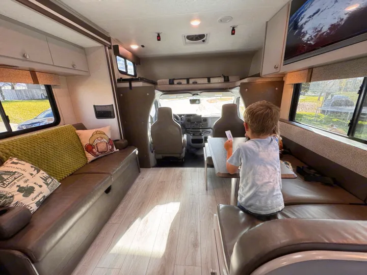 Cozy RV rental interior view, featuring a child at the dinette, comfortable seating, and the driver's cabin—perfect for family adventures.. Forest River Coachmen Freelander 2026