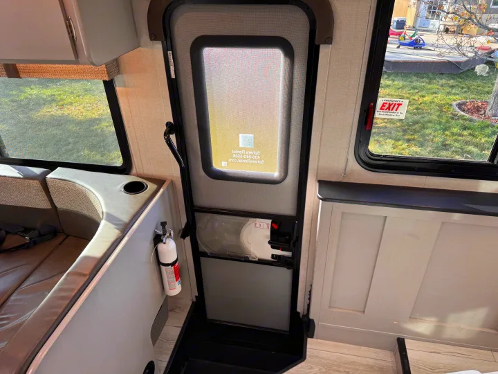 RV rental interior featuring a dinette, main entry door with screen, emergency exit window, and a mounted fire extinguisher.. Forest River Coachmen Freelander 2026