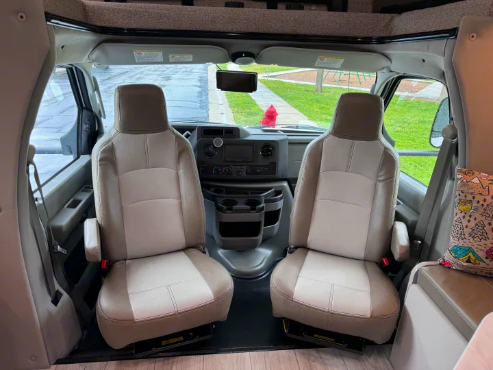 Inside this RV rental: front cabin with comfortable two-tone driver and passenger seats, dashboard, and a clear street view.. Forest River Coachmen Freelander 2026