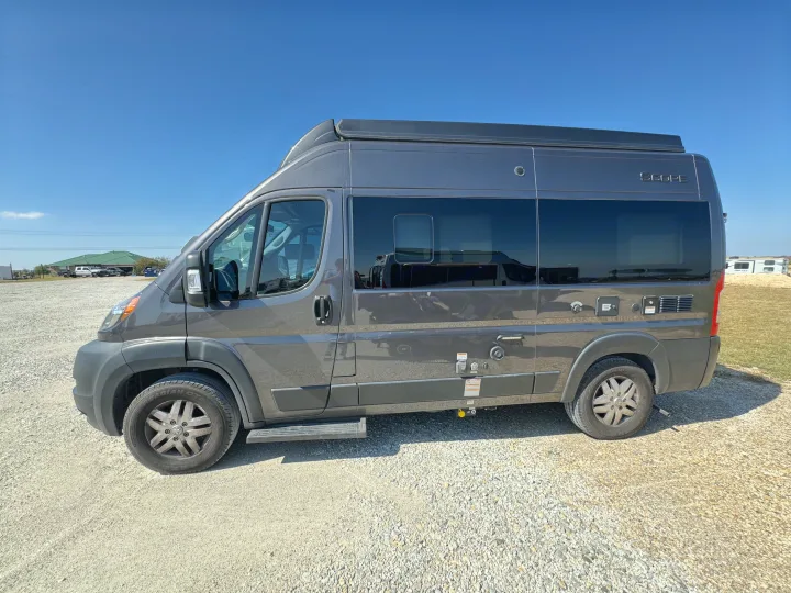 Grey Scope camper van, an RV rental, parked on gravel under a clear blue sky. Ready for your next road trip.. Thor Scope 2023