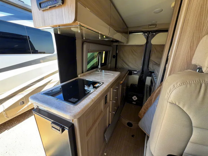 Modern RV rental interior: kitchen with induction stovetop, sink, fridge, and cabinets. Cozy, compact living space.. Thor Scope 2023