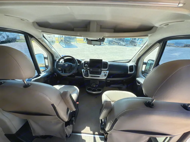 Spacious RV rental cockpit: front seats, modern dashboard, and an outdoor view of other RVs in a lot.. Thor Scope 2023