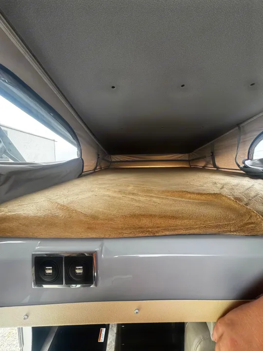 Cozy pop-top RV rental sleeping area: tan bed, mesh windows, and handy USB charging ports for your next adventure.. Thor Scope 2023