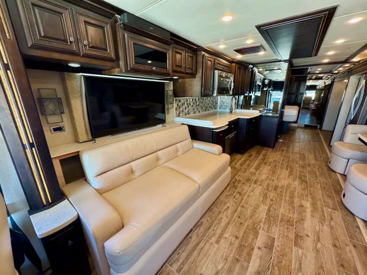 Inside a luxurious RV rental with a comfortable beige sofa, sleek TV, and full kitchen, featuring wood-look tile flooring.. Dutch Star Dutch Star Motorhome 2017
