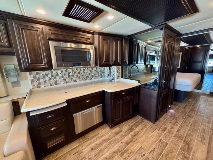 Modern rv rental kitchen with dark wood cabinets, stainless steel appliances, light countertops, and wood-look floor.. Dutch Star Dutch Star Motorhome 2017