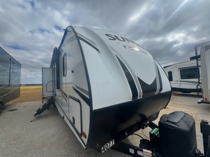 Front view of a white Sunset Trail Super Lite travel trailer RV rental, parked on a gravel lot under a cloudy sky.. Crossroads RV Sunset Trail Super Lite 2022