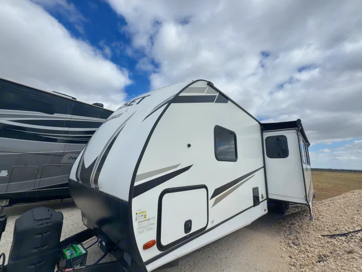 RV rental: White Sunset Trail travel trailer with slide-out, parked on gravel beside another camper under a cloudy sky.. Crossroads RV Sunset Trail Super Lite 2022
