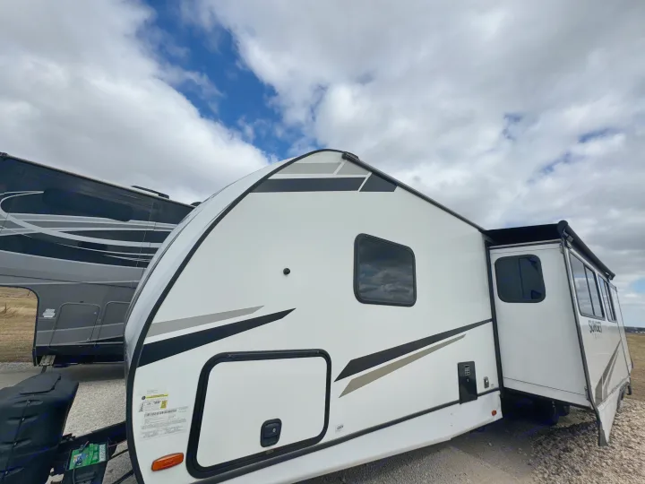 A sleek, white travel trailer RV rental, featuring a rounded front, ready for adventure under a partly cloudy sky.. Crossroads RV Sunset Trail Super Lite 2022