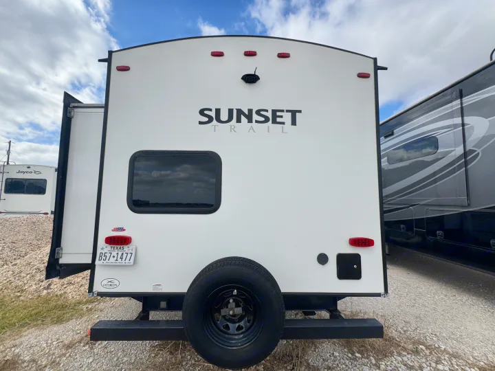 Rear of a white "Sunset Trail" travel trailer rv rental, featuring a spare tire, Texas license plate, and backup camera.. Crossroads RV Sunset Trail Super Lite 2022