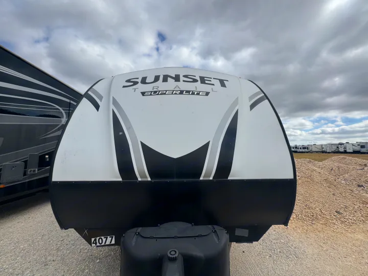 White Sunset Trail Super Lite travel trailer (RV) with black/grey graphics, likely for rv rental, parked on gravel with other RVs nearby.. Crossroads RV Sunset Trail Super Lite 2022