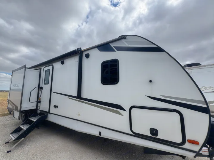 This white travel trailer RV rental, with a deployed awning and steps, is parked on gravel under a cloudy sky.. Crossroads RV Sunset Trail Super Lite 2022