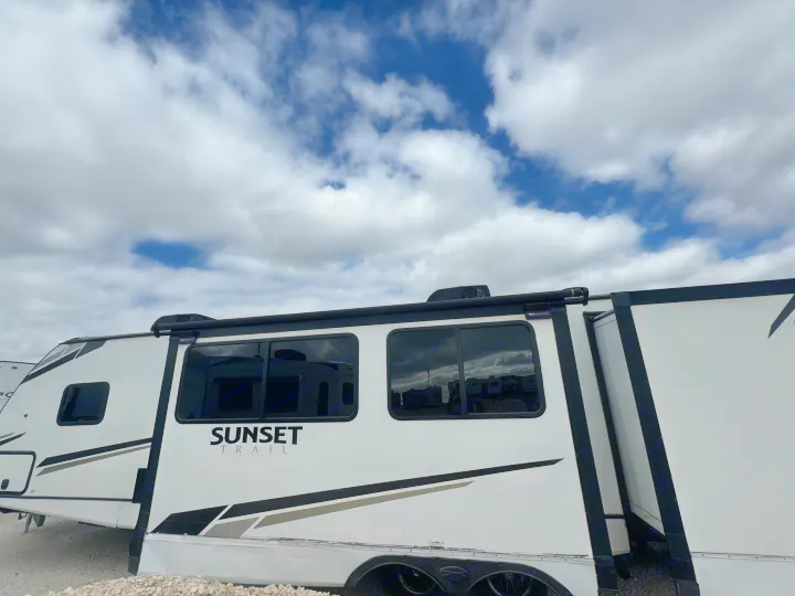 White Sunset Trail travel trailer for rv rental, parked outdoors under a cloudy sky. Shows windows and awning.. Crossroads RV Sunset Trail Super Lite 2022