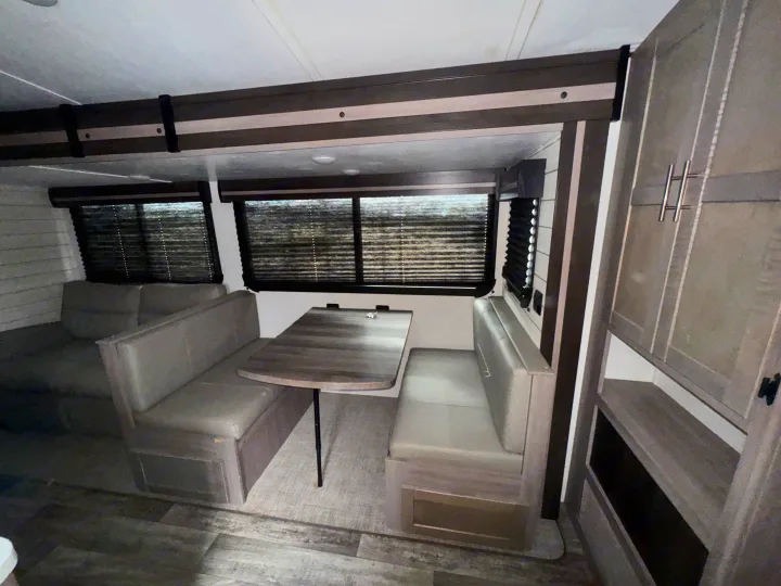 Cozy RV rental dinette featuring a wood table, upholstered benches, and windows with blinds for privacy.. Crossroads RV Sunset Trail Super Lite 2022