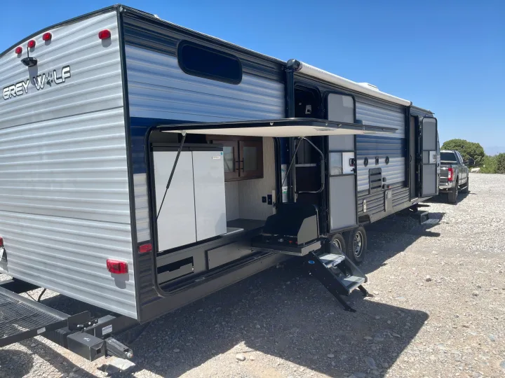 Grey Wolf RV rental with an exterior kitchen featuring a fridge, cooktop, and sink, plus accessible steps and a rear rack.. Forest River Cherokee Grey Wolf 2021