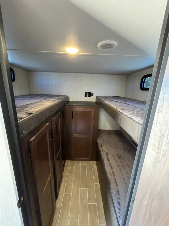 RV rental bunkhouse with four bunk beds (two on each side), central storage cabinets, and wood-look tile flooring.. Forest River Cherokee Grey Wolf 2021