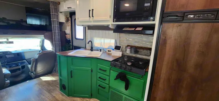This RV rental features a cozy kitchen with green lower cabinets, white uppers, sink, stove, microwave, and driving cockpit.. Jayco Redhawk 2017