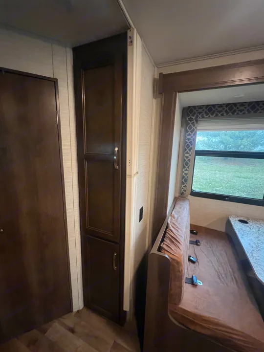 RV rental interior featuring dark wood cabinetry and a dinette with brown cushions by a window, ideal for travel.. Jayco Redhawk 2019