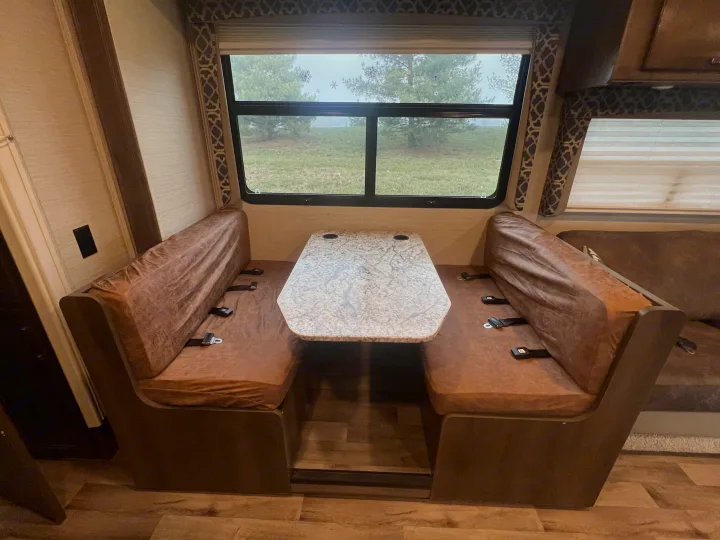 This RV rental features a comfortable dinette with padded benches, seatbelts, and a table, offering an outdoor view.. Jayco Redhawk 2019