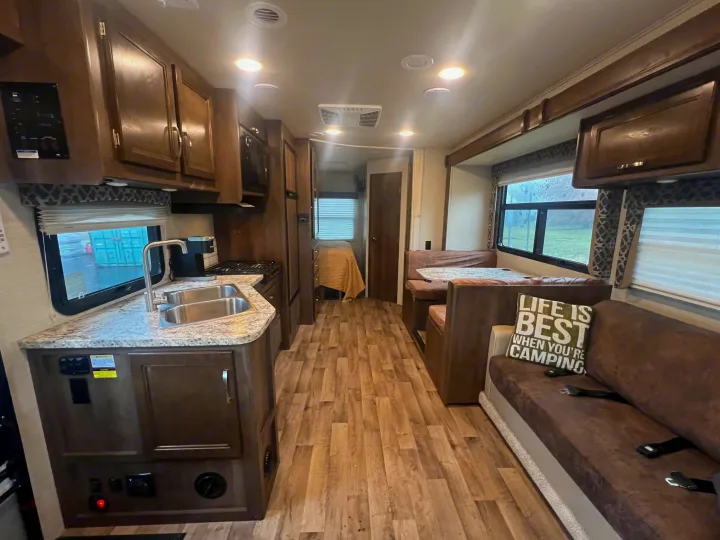 Spacious RV rental interior with a functional kitchen, cozy dining booth, and living area with wood flooring.. Jayco Redhawk 2019