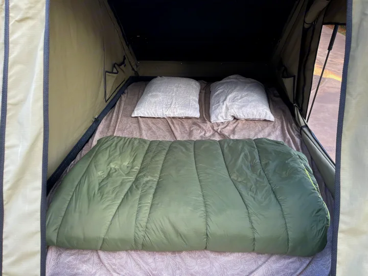 Cozy rv rental rooftop tent interior features a bed with two pillows and a green sleeping bag, ready for adventure.. Jeep Gladiator 2022