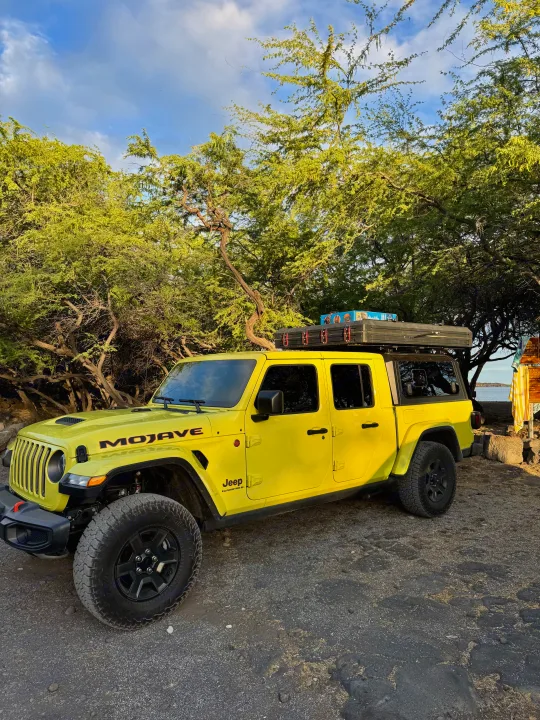 Bright yellow Jeep Gladiator Mojave with a rooftop tent, perfect for an RV rental adventure, parked among trees near the water.. jeep Gladiator 2023