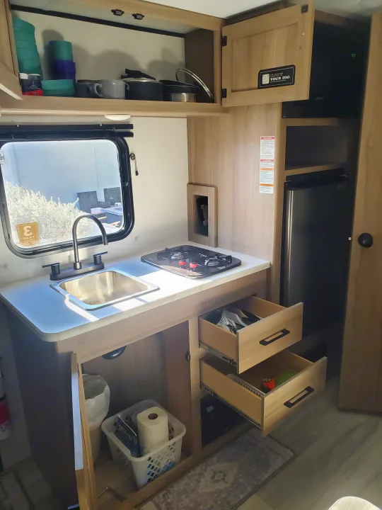 Inside a clean **rv rental** kitchen, showing a sink, two-burner stove, microwave, fridge, and open drawers with utensils.. Keystone Coleman 2026