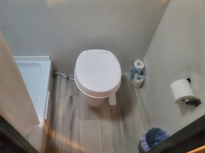 Compact RV rental bathroom: white toilet, adjacent shower, and toilet paper (on holder & spare rolls).. Keystone Coleman 2026