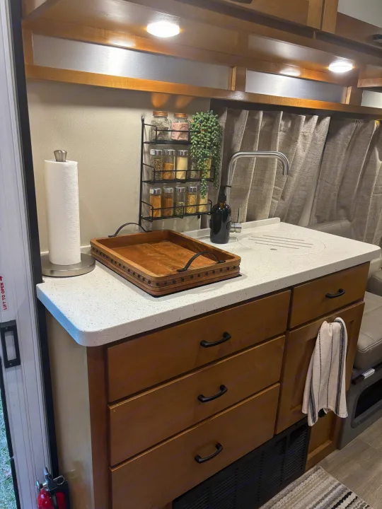 This organized RV rental kitchen features white counters, a compact sink, spice rack, and wooden cabinetry, optimized for travel.. Coachmen Beyond 22C 2020