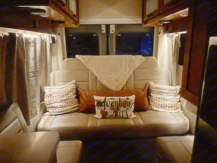 Cozy rv rental seating with "Adventure Awaits" pillow & blanket, ready for a night's rest. Curtains drawn in the low light.. Coachmen Beyond 22C 2020