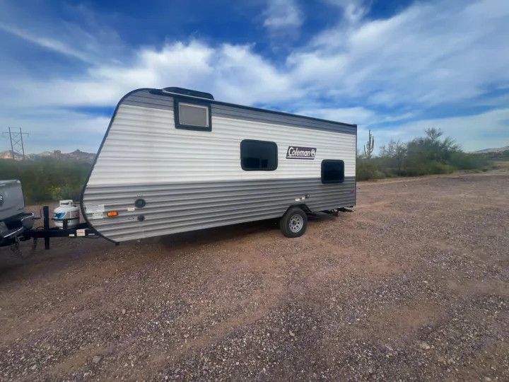 This Coleman RV rental is parked on a gravel lot in the desert, under a cloudy sky with distant mountains.. Coleman Coleman 2023