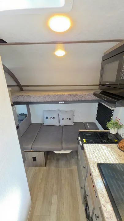 Cozy rv rental interior featuring a bunk bed, a dinette area with "GO PLAY" pillows, and a compact kitchen.. Wayfinder RV Go Lite 2025
