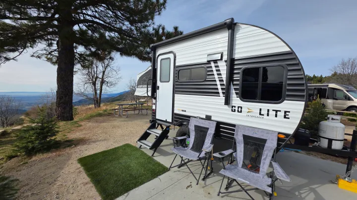 A Go Lite travel trailer rv rental is set up with chairs at a scenic mountain campsite, offering panoramic views.. Wayfinder RV Go Lite 2025