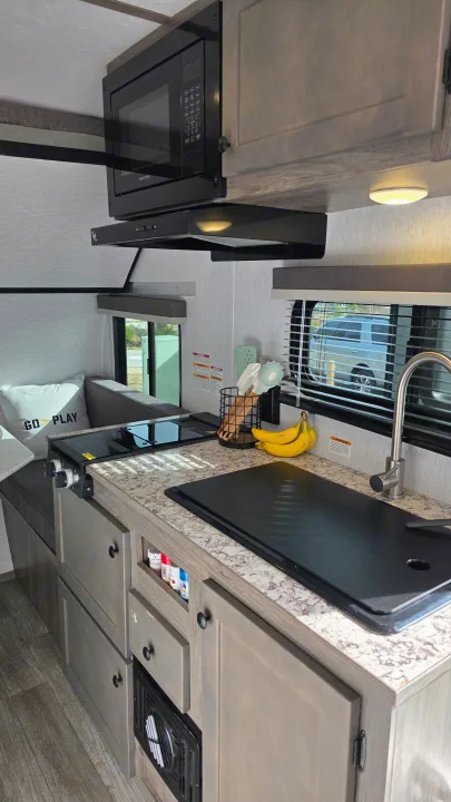 Explore this rv rental's compact kitchen, featuring a microwave, cooktop, covered sink, and wood-toned cabinets.. Wayfinder RV Go Lite 2025