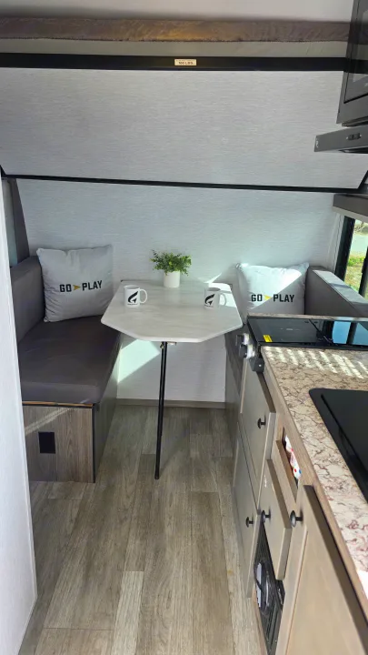 RV rental interior: dinette with 'GO PLAY' pillows, compact kitchen, and overhead bunk bed, ready for adventure.. Wayfinder RV Go Lite 2025