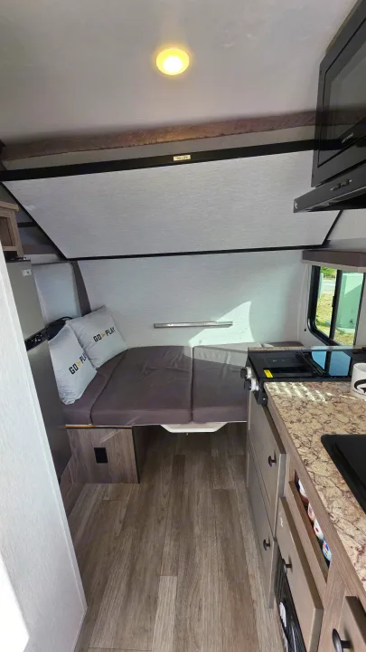 Compact rv rental interior shows a bed, kitchen with stovetop & microwave, plus a 100-lb capacity bunk. Ready for adventure!. Wayfinder RV Go Lite 2025