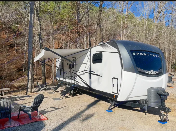 SportTrek RV rental parked in a sunny, tree-lined campsite with an extended awning and outdoor seating. Perfect for a nature escape.. Venture Rv SPORTTREK TOURING EDITION 2025