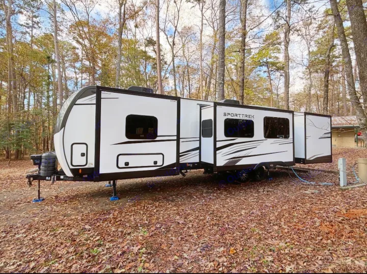 White SportTrek RV rental with extended slide-outs, set up on a leaf-covered campsite under tall trees, ready for nature.. Venture Rv SPORTTREK TOURING EDITION 2025