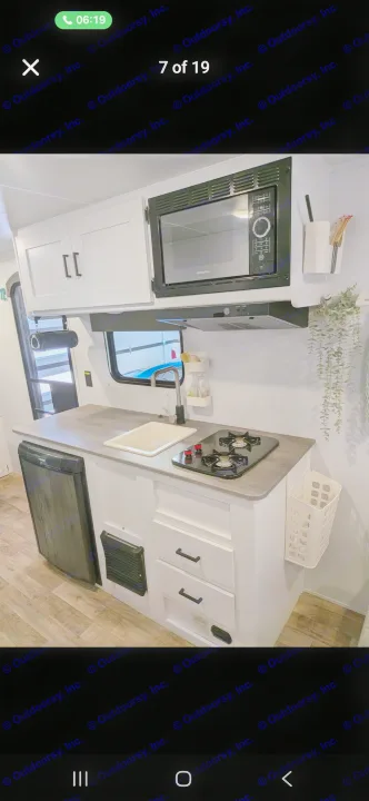 This rv rental features a compact kitchen with white cabinets, microwave, sink, two-burner stove, and small fridge.. Keystone RV Hideout 2022