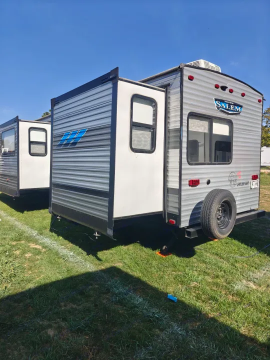 Two modern RVs with extended slide-outs, gray and white, parked on green grass under a blue sky, ready for rv rental.. Salem 36VBDS 2021