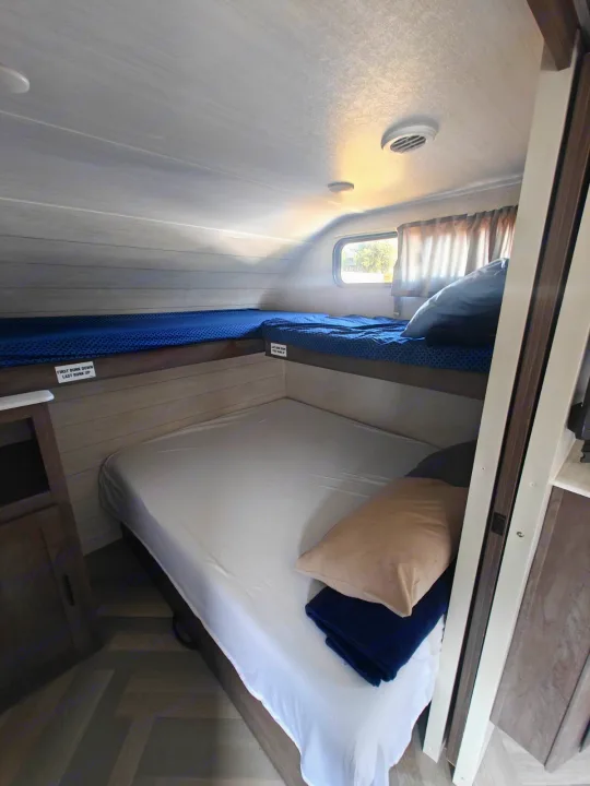 Spacious RV rental sleeping area featuring three bunk beds with blue and white bedding, a window, and wood-look walls.. Salem 36VBDS 2021