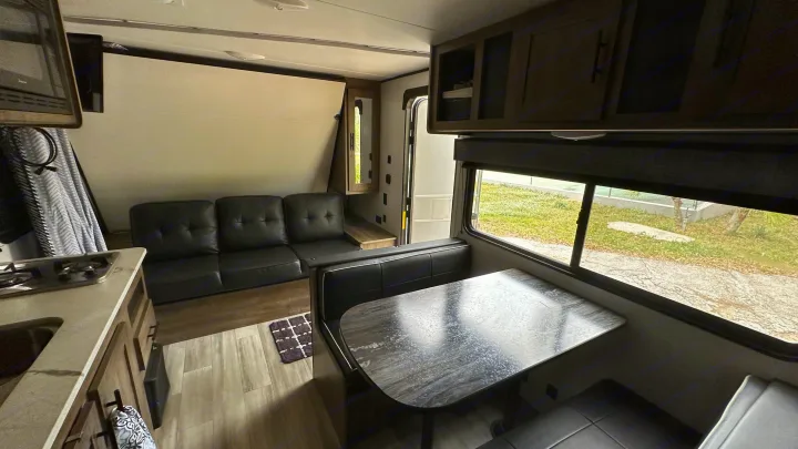 RV rental interior featuring a compact kitchen, adaptable sofa bed, and dinette by a large window, offering a comfortable travel living space.. Heartland RVs Pioneer Trail Blazer 2022