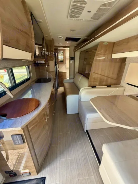 Spacious RV rental interior: modern kitchenette with TV, sofa, and dinette. Features light wood cabinetry and tile flooring.. Jayco Melbourne Prestige 2023