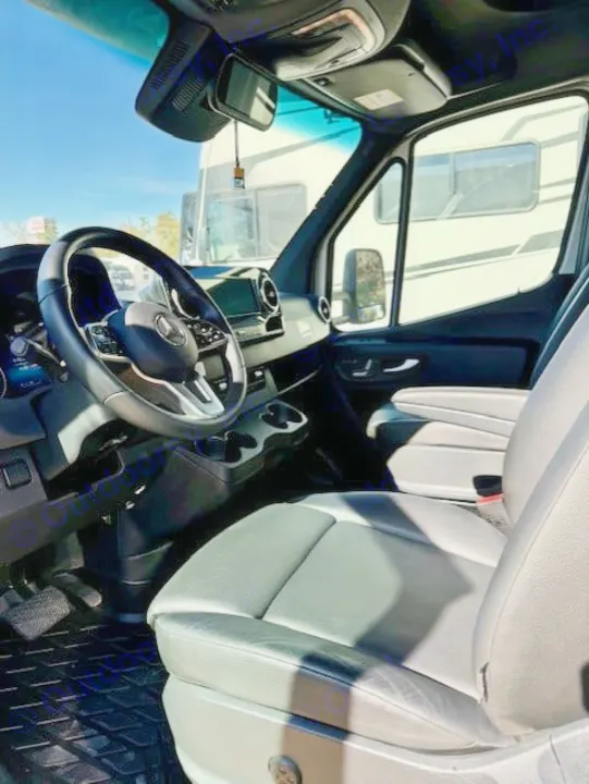 Inside this RV rental: View from the passenger side showing the driver's seat, steering wheel, and dashboard. Another RV is seen outside.. Jayco Melbourne Prestige 2023
