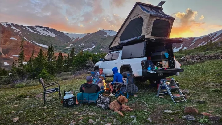 Scenic mountain camping adventure with an RV rental. A group with their dog enjoys a campfire at sunset.. Toyota Tacoma 2018