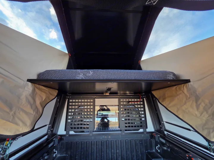 Inside a truck bed camper, showing the mattress and cargo grid. Perfect for your next RV rental adventure!. Toyota Tacoma 2018