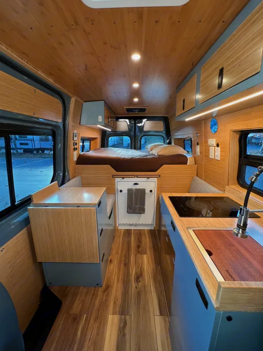 Modern **rv rental** interior: a cozy camper van with a wooden ceiling, built-in bed, kitchenette, and dining area.. Mercedes-Benz Sprinter 2024
